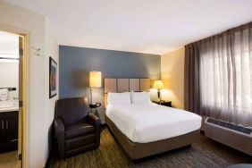 Sonesta Simply Suites St Louis Earth City double bed guest room, featuring armchair, window, and ensuite bathroom.