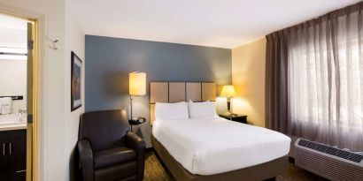 Sonesta Simply Suites St Louis Earth City double bed guest room, featuring armchair, window, and ensuite bathroom.