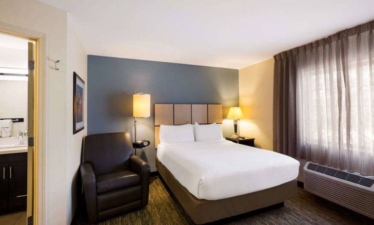 Sonesta Simply Suites St Louis Earth City double bed guest room, featuring armchair, window, and ensuite bathroom.