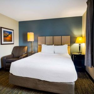 Sonesta Simply Suites St Louis Earth City double bed guest room, featuring bedside lamps, window, and armchair.