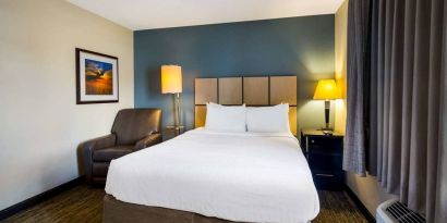 Sonesta Simply Suites St Louis Earth City double bed guest room, featuring bedside lamps, window, and armchair.