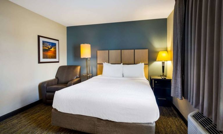 Sonesta Simply Suites St Louis Earth City double bed guest room, featuring bedside lamps, window, and armchair.