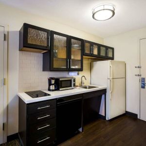 Sonesta Simply Suites St Louis Earth City guest room kitchen, complete with array of cupboards and drawers, plus a hob, microwave, and fridge-freezer.