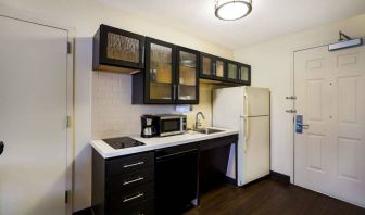 Sonesta Simply Suites St Louis Earth City guest room kitchen, complete with array of cupboards and drawers, plus a hob, microwave, and fridge-freezer.