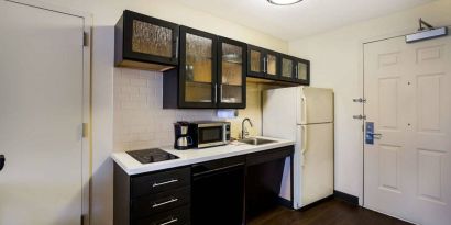 Sonesta Simply Suites St Louis Earth City guest room kitchen, complete with array of cupboards and drawers, plus a hob, microwave, and fridge-freezer.