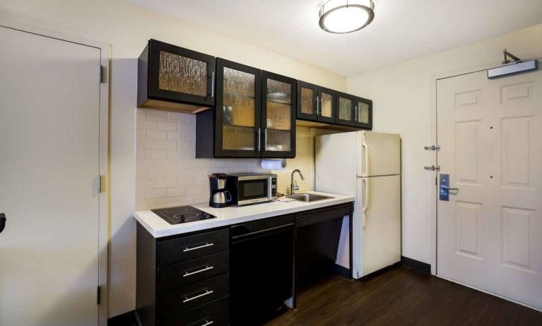 Sonesta Simply Suites St Louis Earth City guest room kitchen, complete with array of cupboards and drawers, plus a hob, microwave, and fridge-freezer.