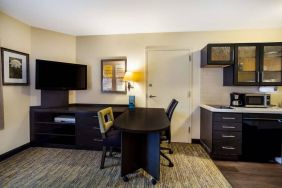 Sonesta Simply Suites St Louis Earth City guest room workspace, furnished with desk and chairs, with TV and kitchen nearby.