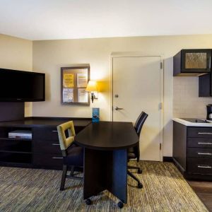 Sonesta Simply Suites St Louis Earth City guest room workspace, furnished with desk and chairs, with TV and kitchen nearby.