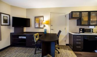 Sonesta Simply Suites St Louis Earth City guest room workspace, furnished with desk and chairs, with TV and kitchen nearby.