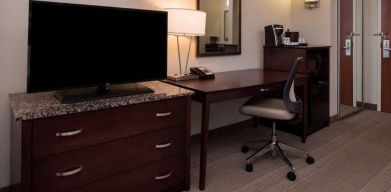 Sonesta Chicago O'Hare Airport Rosemont guest room workspace, including desk, chair, lamp, telephone, and nearby TV.