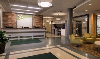 The hotel lobby has yellow armchairs, potted plants, and a business center workstation, in addition to the reception desk.