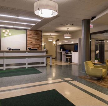 The hotel lobby has yellow armchairs, potted plants, and a business center workstation, in addition to the reception desk.