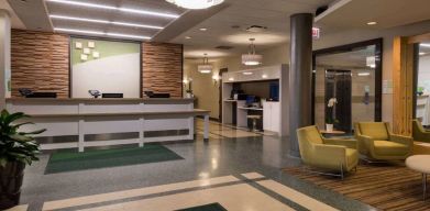 The hotel lobby has yellow armchairs, potted plants, and a business center workstation, in addition to the reception desk.