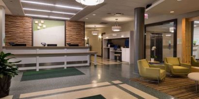 The hotel lobby has yellow armchairs, potted plants, and a business center workstation, in addition to the reception desk.