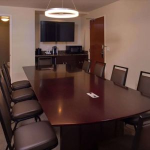 Meeting room in Sonesta Chicago O'Hare Airport Rosemont, featuring long wooden table, 10 chairs, a microwave, and a large TV.