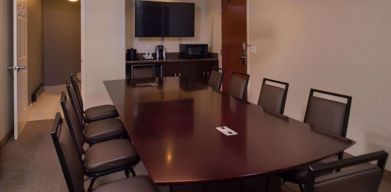 Meeting room in Sonesta Chicago O'Hare Airport Rosemont, featuring long wooden table, 10 chairs, a microwave, and a large TV.