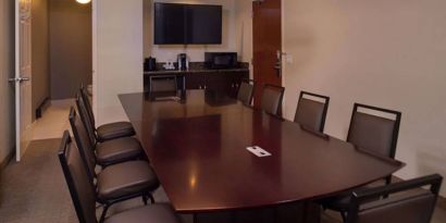 Meeting room in Sonesta Chicago O'Hare Airport Rosemont, featuring long wooden table, 10 chairs, a microwave, and a large TV.