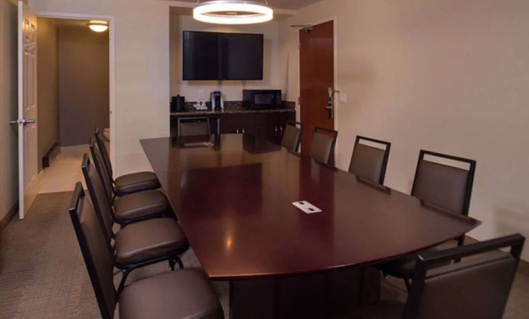 Meeting room in Sonesta Chicago O'Hare Airport Rosemont, featuring long wooden table, 10 chairs, a microwave, and a large TV.