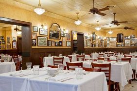 The hotel restaurant has white tablecloths, ceiling fans, and walls brimming with mirrors and photographs.