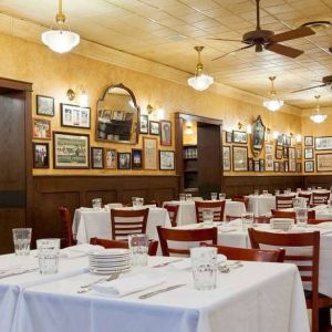 The hotel restaurant has white tablecloths, ceiling fans, and walls brimming with mirrors and photographs.