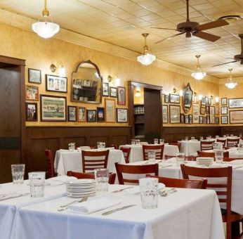 The hotel restaurant has white tablecloths, ceiling fans, and walls brimming with mirrors and photographs.