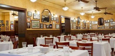 The hotel restaurant has white tablecloths, ceiling fans, and walls brimming with mirrors and photographs.