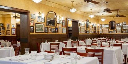 The hotel restaurant has white tablecloths, ceiling fans, and walls brimming with mirrors and photographs.