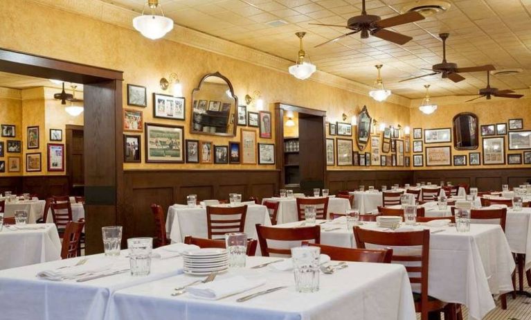 The hotel restaurant has white tablecloths, ceiling fans, and walls brimming with mirrors and photographs.