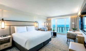 Royal Sonesta San Juan double bed guest room, furnished with table and chairs, sofa and coffee table, and a a balcony with ocean views.