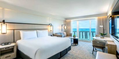 Royal Sonesta San Juan double bed guest room, furnished with table and chairs, sofa and coffee table, and a a balcony with ocean views.