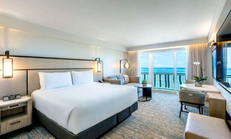 Royal Sonesta San Juan double bed guest room, furnished with table and chairs, sofa and coffee table, and a a balcony with ocean views.