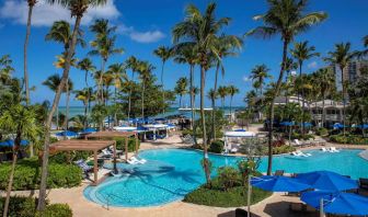 Royal Sonesta San Juan’s outdoor pool features sun loungers by the side and in shallow water, with towering palm trees all around.