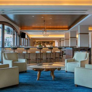 Royal Sonesta San Juan’s lobby lounge has a quartet of armchairs around a coffee table, with a wall-mounted TV and nearby bar.