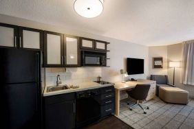 Sonesta Simply Suites Jersey City guest room kitchen, with microwave, oven, hob, and fridge-freezer, plus nearby chair and TV.