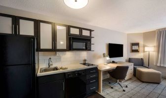 Sonesta Simply Suites Jersey City guest room kitchen, with microwave, oven, hob, and fridge-freezer, plus nearby chair and TV.