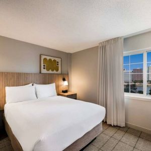 Double bed guest room in Sonesta Simply Suites Jersey City, including art on the wall, TV, and window.