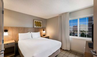 Double bed guest room in Sonesta Simply Suites Jersey City, including art on the wall, TV, and window.