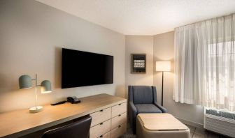 Sonesta Simply Suites Jersey City guest room workspace, including desk, chair, and lamp, with nearby TV and armchair.