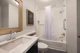 Guest bathroom in Sonesta Simply Suites Jersey City, furnished with bath and shower, lavatory, and sink and mirror.