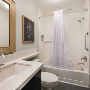 Guest bathroom in Sonesta Simply Suites Jersey City, furnished with bath and shower, lavatory, and sink and mirror.