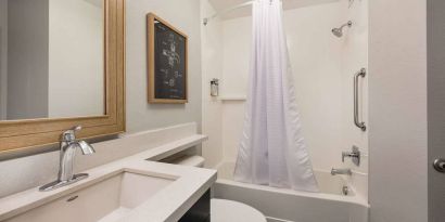 Guest bathroom in Sonesta Simply Suites Jersey City, furnished with bath and shower, lavatory, and sink and mirror.