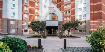 The hotel’s exterior has a brickwork surface, with flowers and trees either side of the entrance, which has the Sonesta Simply Suites name on it.