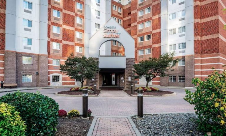 The hotel’s exterior has a brickwork surface, with flowers and trees either side of the entrance, which has the Sonesta Simply Suites name on it.