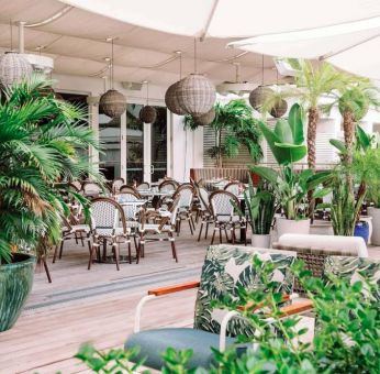 The hotel offers outdoor dining, with an abundance of plant life around the tables for four.