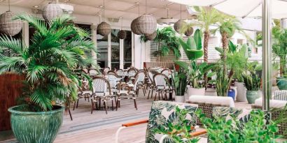 The hotel offers outdoor dining, with an abundance of plant life around the tables for four.