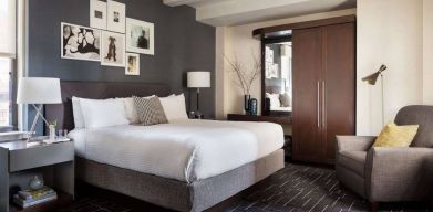 Double bed guest room in The Shelburne Sonesta New York, furnished with bedside lamp, wardrobe, and armchair.