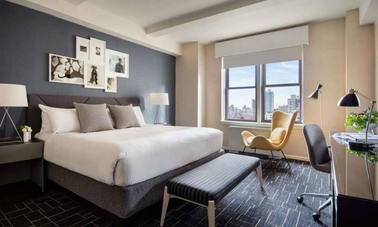 Double bed guest room in The Shelburne Sonesta New York, featuring a window, art on the wall, and a workspace desk, chair, and lamp.