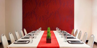 Meeting room in The Shelburne Sonesta New York, furnished with long table, 10 chairs around it, and a stark white and red color scheme.