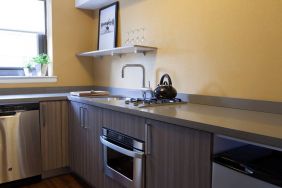 Guest room kitchen in The Fifty Sonesta Select New York, including oven, hob, chopping board, sink, and a small potted plant.