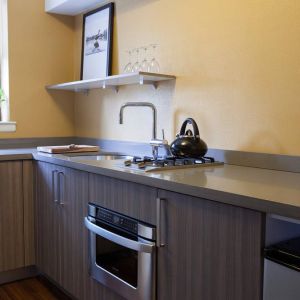 Guest room kitchen in The Fifty Sonesta Select New York, including oven, hob, chopping board, sink, and a small potted plant.